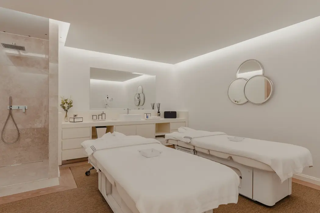 Salle de soins spa de luxe avec deux tables de massage, une décoration minimaliste, un éclairage doux et une douche à l’italienne moderne.