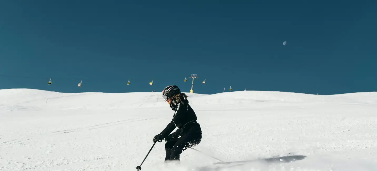 A skier carves through fresh snow under a clear blue sky on a pristine alpine slope.
