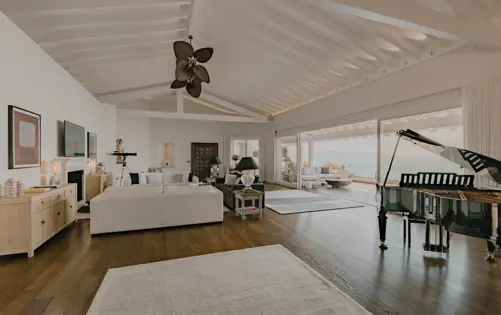 غرفة معيشة فسيحة بتصميم أنيق وسقف مرتفع وإطلالات بانورامية على البحر من النوافذ الممتدة من الأرض حتى السقف.