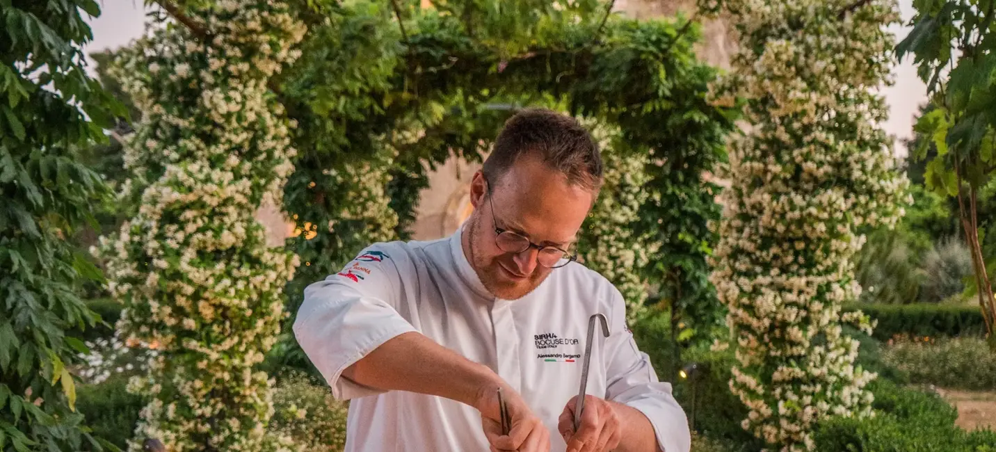 Gourmet chef preparing pasta in a wheel of cheese at an elegant outdoor dining setting.