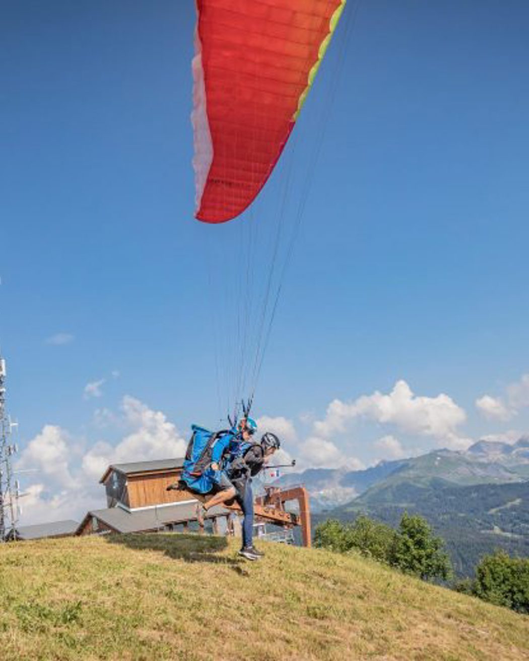 Paraglider taking off from a mountain slope with a red canopy and scenic alpine landscape in the background.