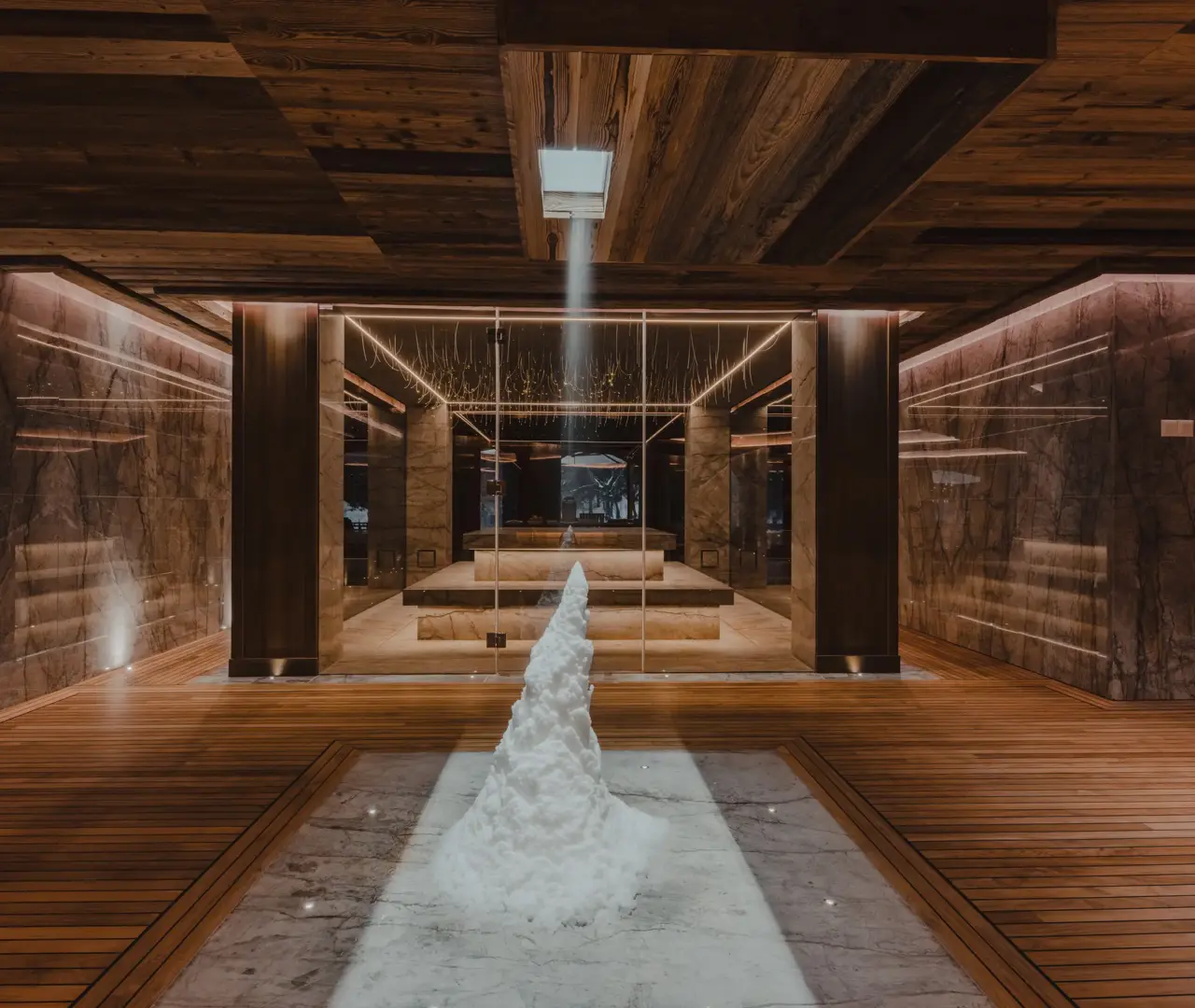 Elegant wellness spa room with marble walls, wooden floors, and a snow fountain under soft ambient lighting in a luxury mountain chalet.