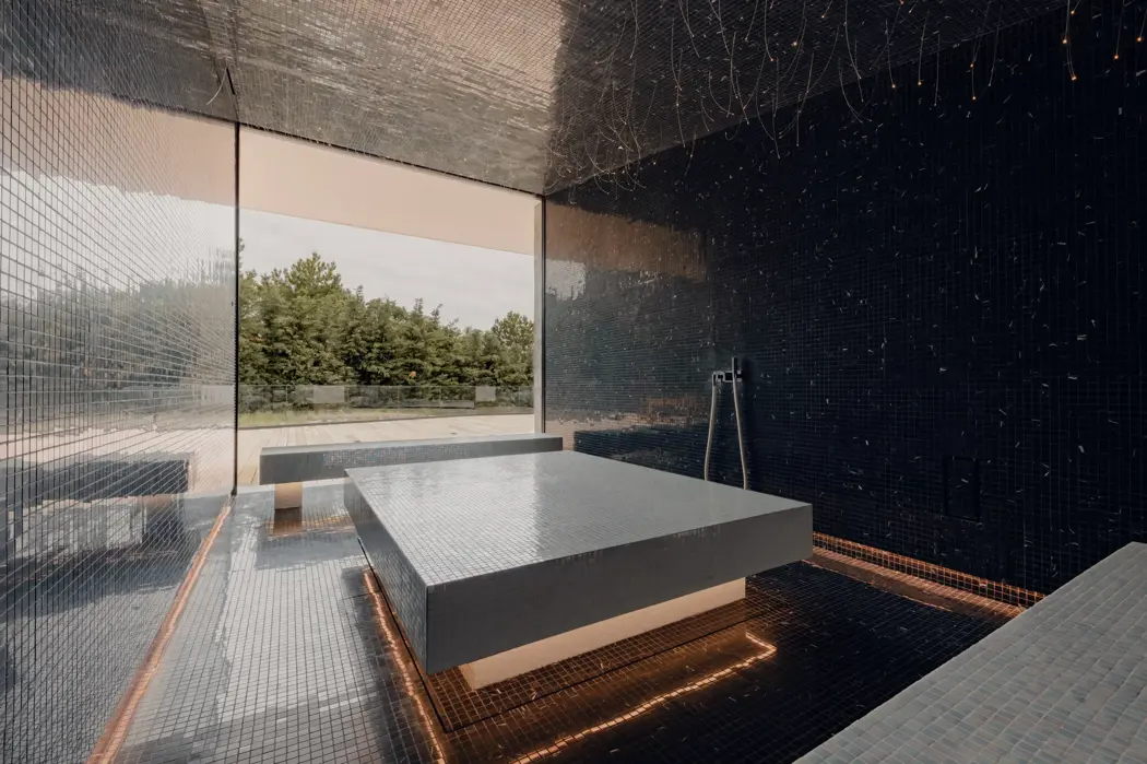 Роскошная спа-комната с мозаичной отделкой, подогреваемым каменным столом, мягким освещением и панорамным окном с видом на террасу и природу.