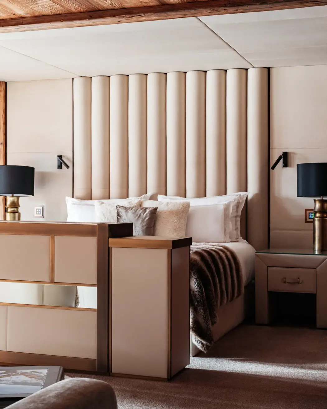 Elegant bedroom with a modern design, featuring a tall padded headboard, plush pillows, and warm neutral tones accented by brass bedside lamps and wooden textures.