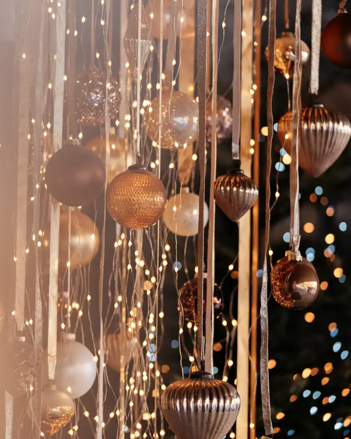 Close-up of elegant Christmas decorations with golden baubles and warm string lights hanging from ribbons, creating a festive and cozy atmosphere.