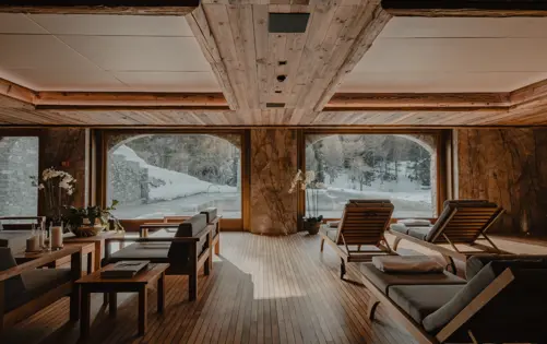 Elegant alpine spa lounge with wooden interiors, large windows overlooking snowy mountains, and cozy relaxation chairs.