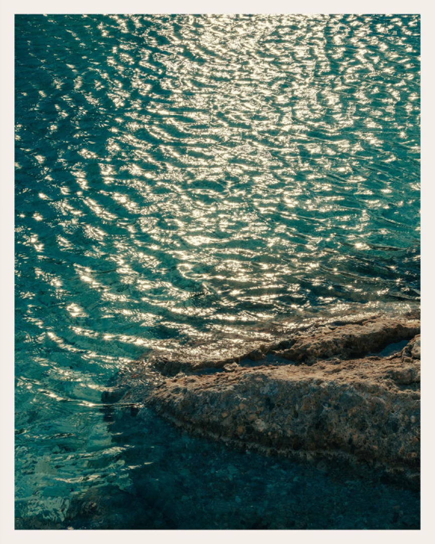 Sunlight reflecting on turquoise sea water near rocky shore.