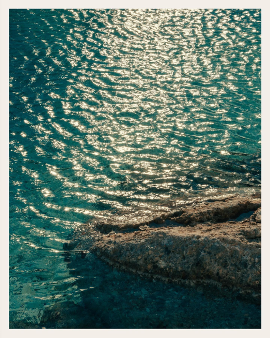 Sunlight reflecting on turquoise sea water near rocky shore.