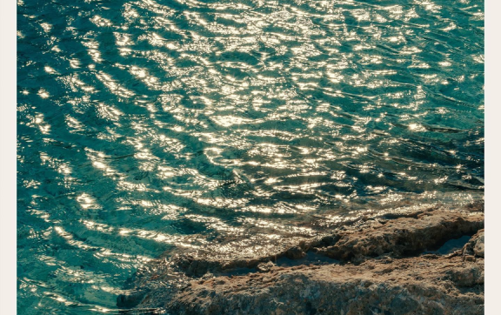 Sunlight reflecting on turquoise sea water near rocky shore.
