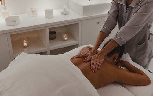 Therapist performing a relaxing back massage in a serene spa treatment room with soft lighting and candles.