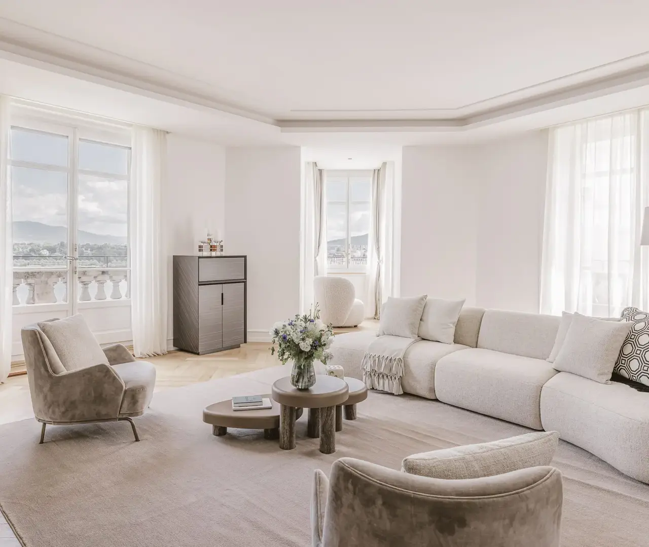 Salon élégant et lumineux avec vue panoramique, doté d’un canapé ivoire incurvé, de fauteuils en velours et d’une palette neutre apaisante. L’espace marie minimalisme contemporain et confort raffiné sous une lumière naturelle abondante.