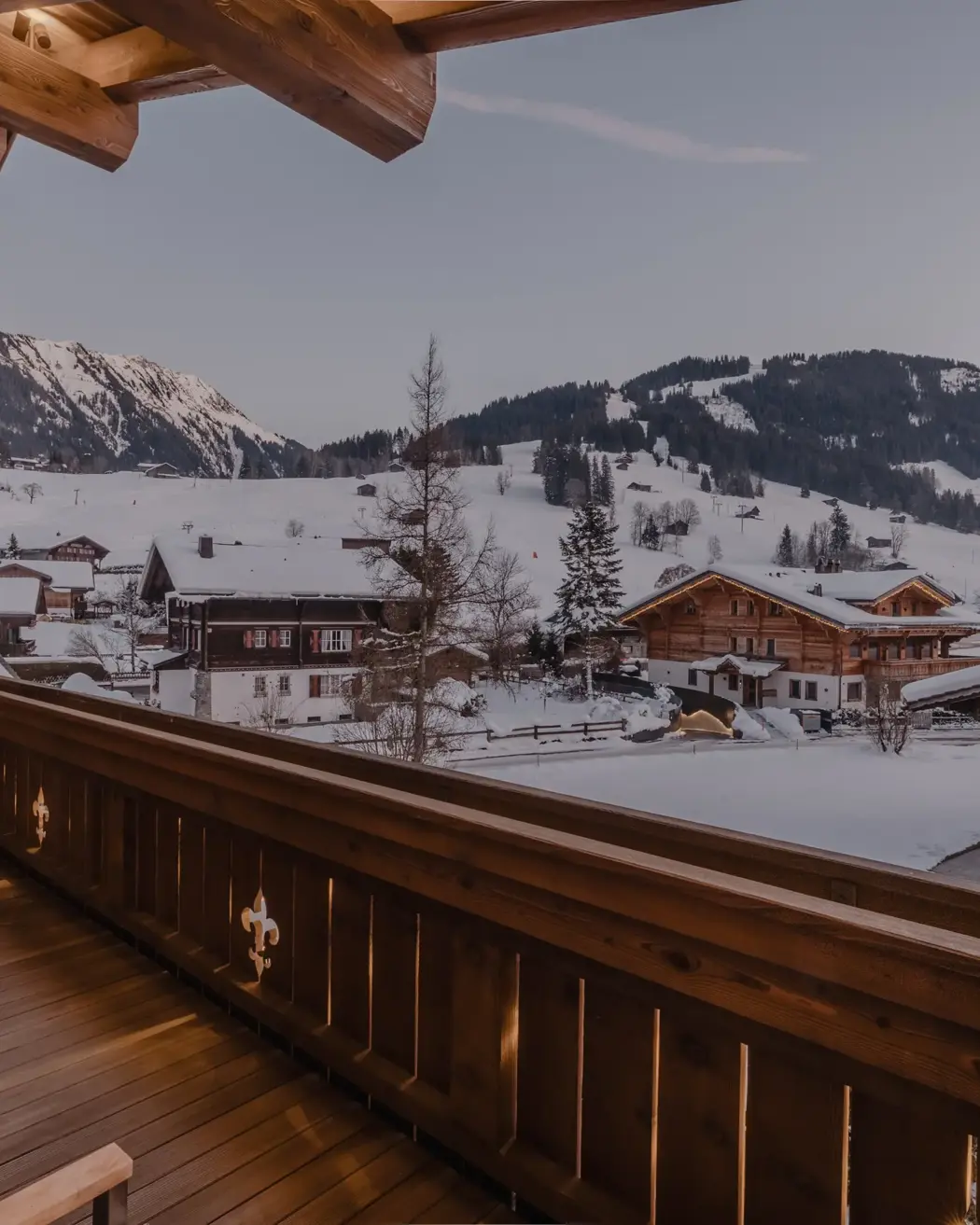 شرفة شاليه عند الغسق تطل على أسطح مغطاة بالثلوج ومنحدرات جبلية.