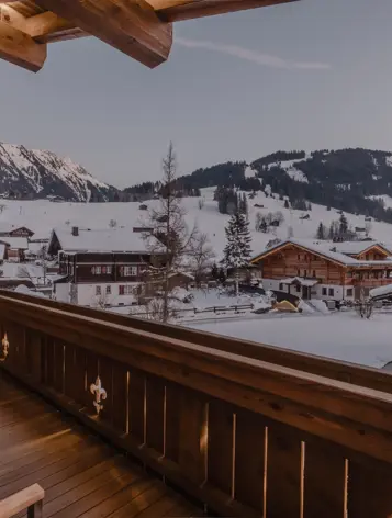Chalet balcony view at dusk overlooking snowy alpine rooftops and mountain slopes.