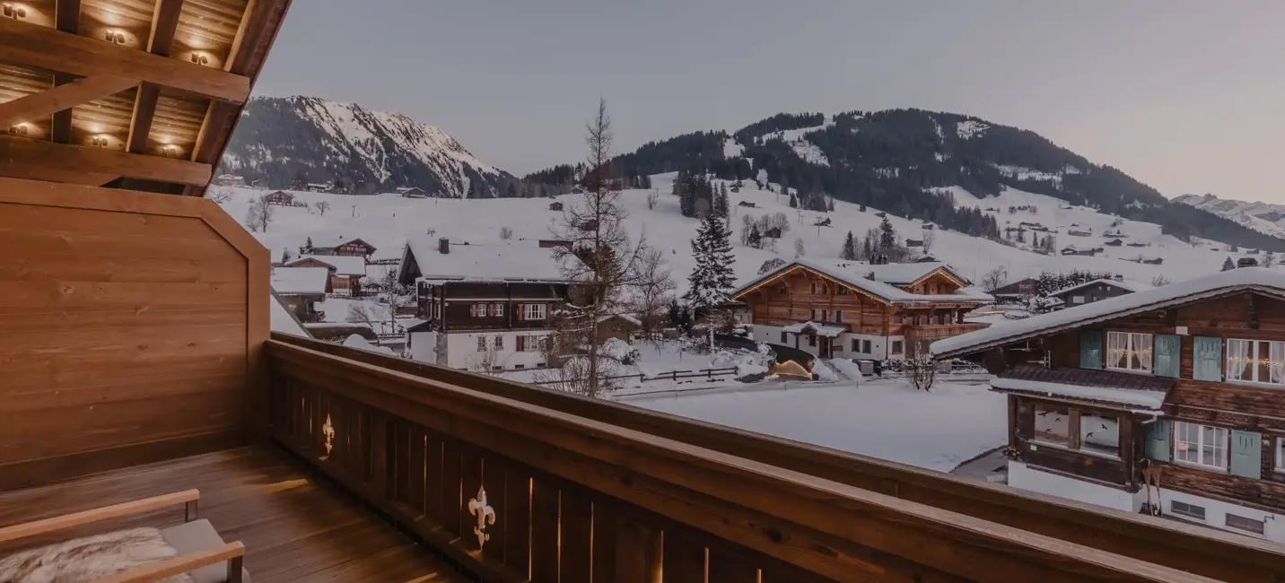 Chalet balcony view at dusk overlooking snowy alpine rooftops and mountain slopes.