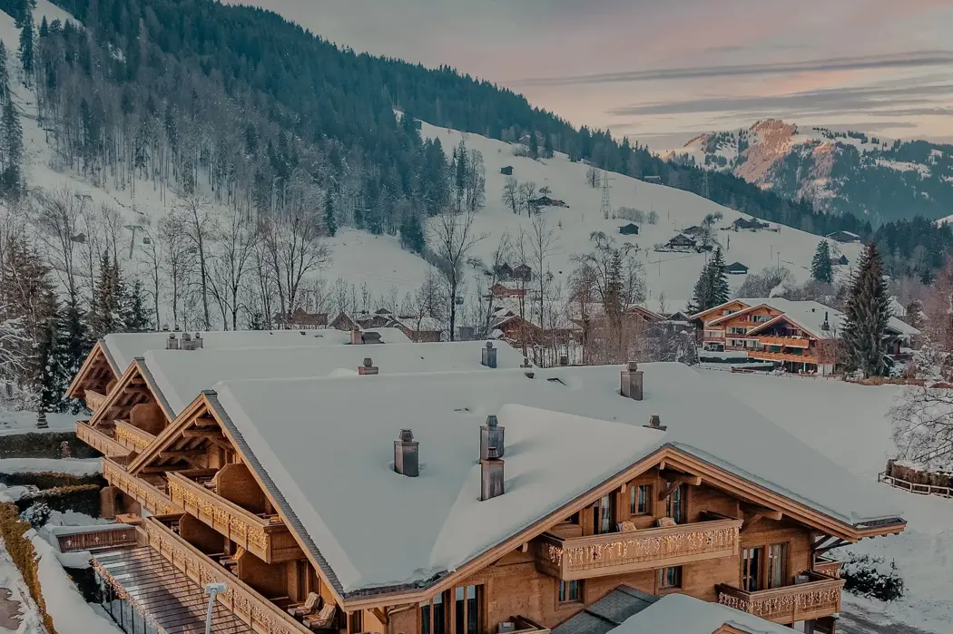 Роскошное деревянное шале, покрытое снегом на закате, расположено в тихой альпийской долине, окружённой горами, покрытыми соснами.