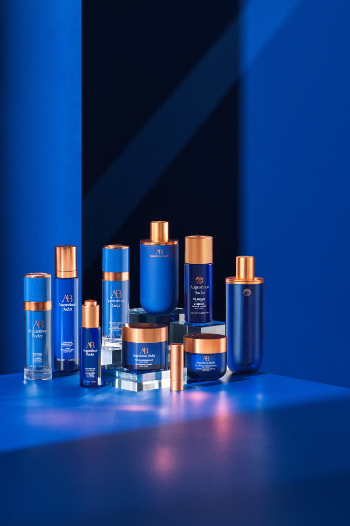 Collection of blue and gold luxury skincare bottles and jars arranged on a glossy blue surface with minimalist lighting and shadows, creating an elegant, modern presentation.
