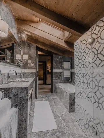 A refined marble bathroom with intricate patterned glass, wooden ceiling beams, and elegant lighting. The space blends natural textures with modern sophistication.