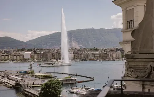 Panoramic view of Geneva’s Jet d’Eau fountain rising above Lake Geneva, surrounded by elegant waterfront architecture and moored sailboats, with the Jura mountains in the distance. A timeless symbol of the city, this view embodies refined Swiss living and lakeside serenity.