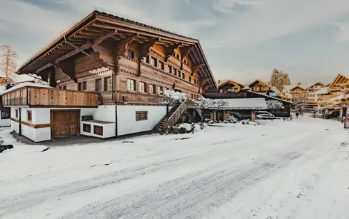 Chalet alpin traditionnel avec architecture en bois sculpté dans un village de montagne enneigé par une journée d’hiver ensoleillée.