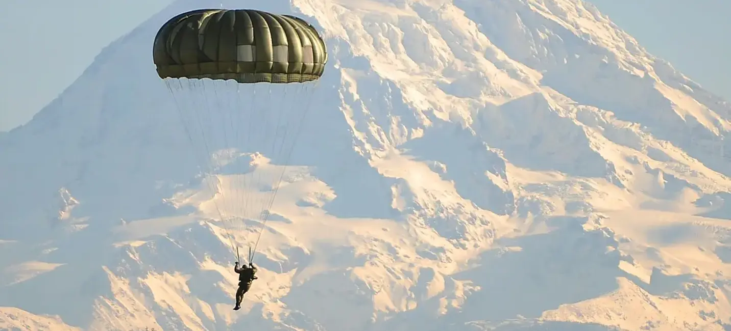 مظلي وحيد يهبط عبر هواء جبلي صافٍ، والقمم المغطاة بالثلوج ترتفع في الأفق – مشهد يجسد الحرية والدقة وروح المغامرة الجبلية.