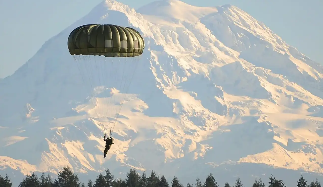 Un parachutiste solitaire descend dans l’air pur des Alpes, face aux sommets enneigés — une scène de liberté, de précision et d’aventure en montagne.