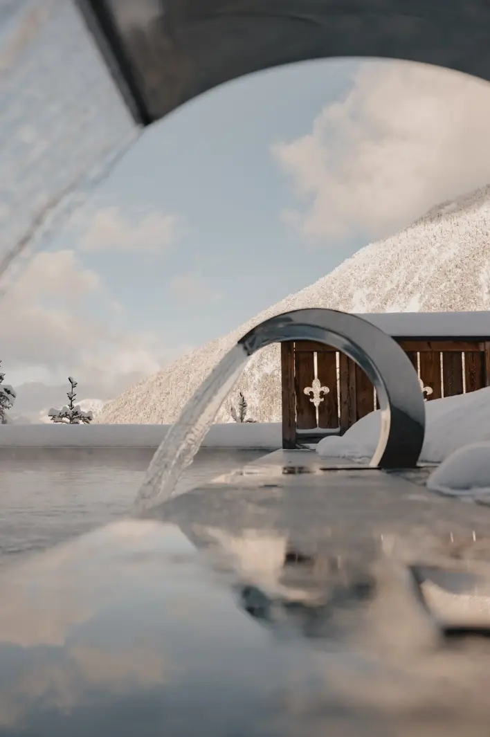 Piscine extérieure chauffée avec fontaines modernes, offrant une vue sur les montagnes enneigées sous un ciel d’hiver dégagé.