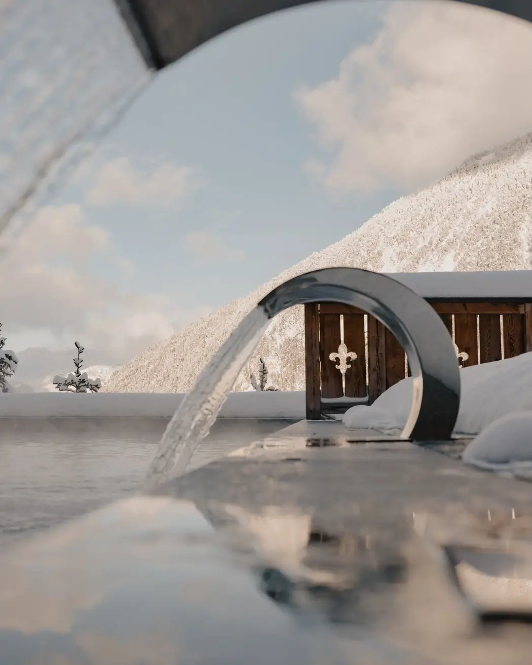 Piscine extérieure chauffée avec fontaines modernes, offrant une vue sur les montagnes enneigées sous un ciel d’hiver dégagé.