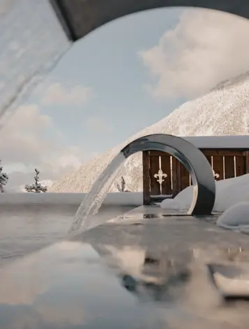 Piscine extérieure chauffée avec fontaines modernes, offrant une vue sur les montagnes enneigées sous un ciel d’hiver dégagé.