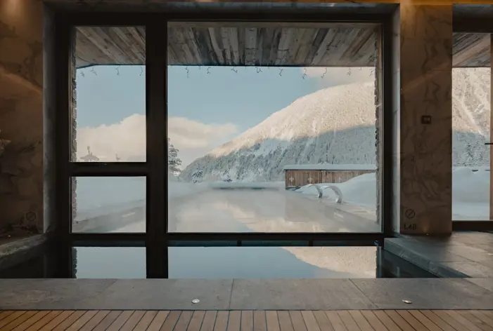A serene mountain spa pool overlooking snowy peaks through floor-to-ceiling windows.