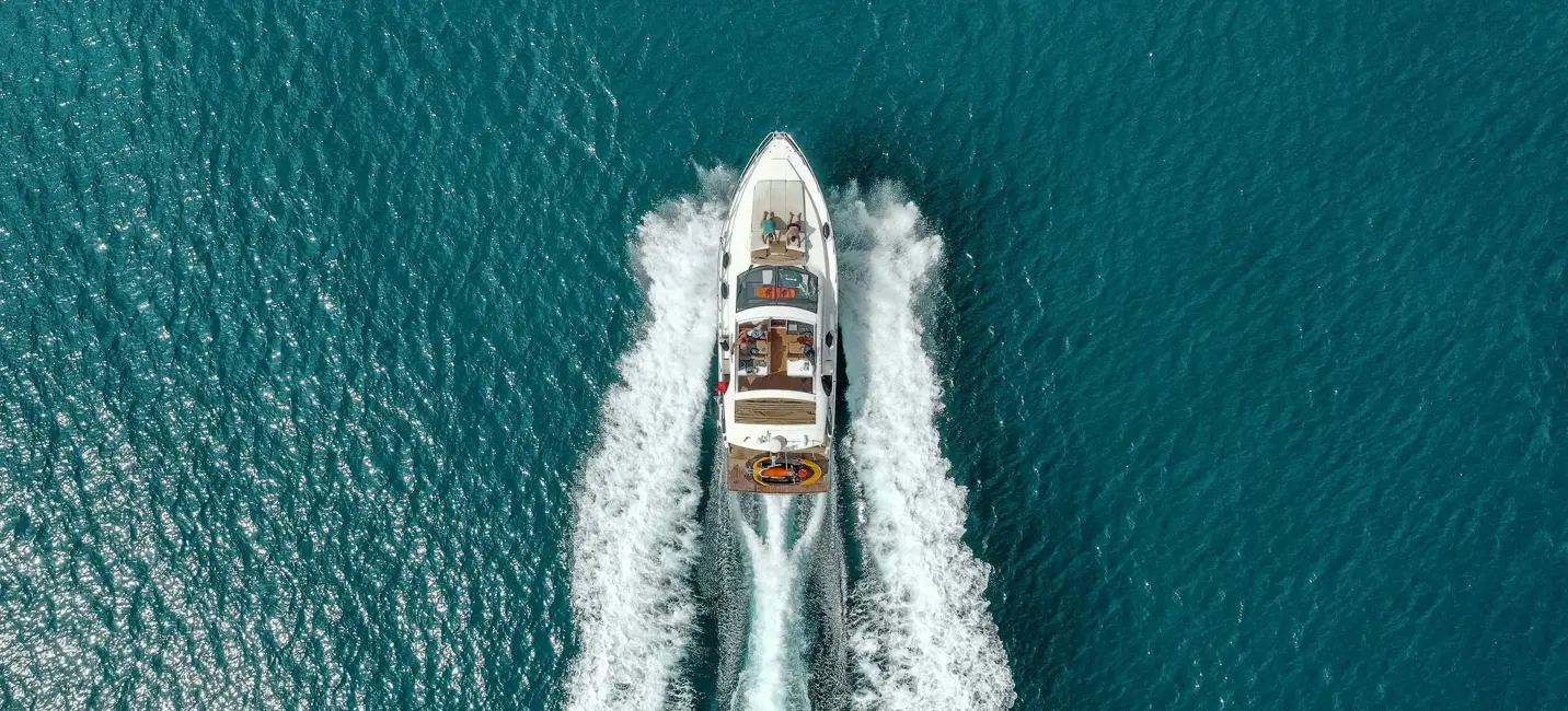 Yacht cruising over deep-turquoise water, white wake trailing behind, on a bright clear day.