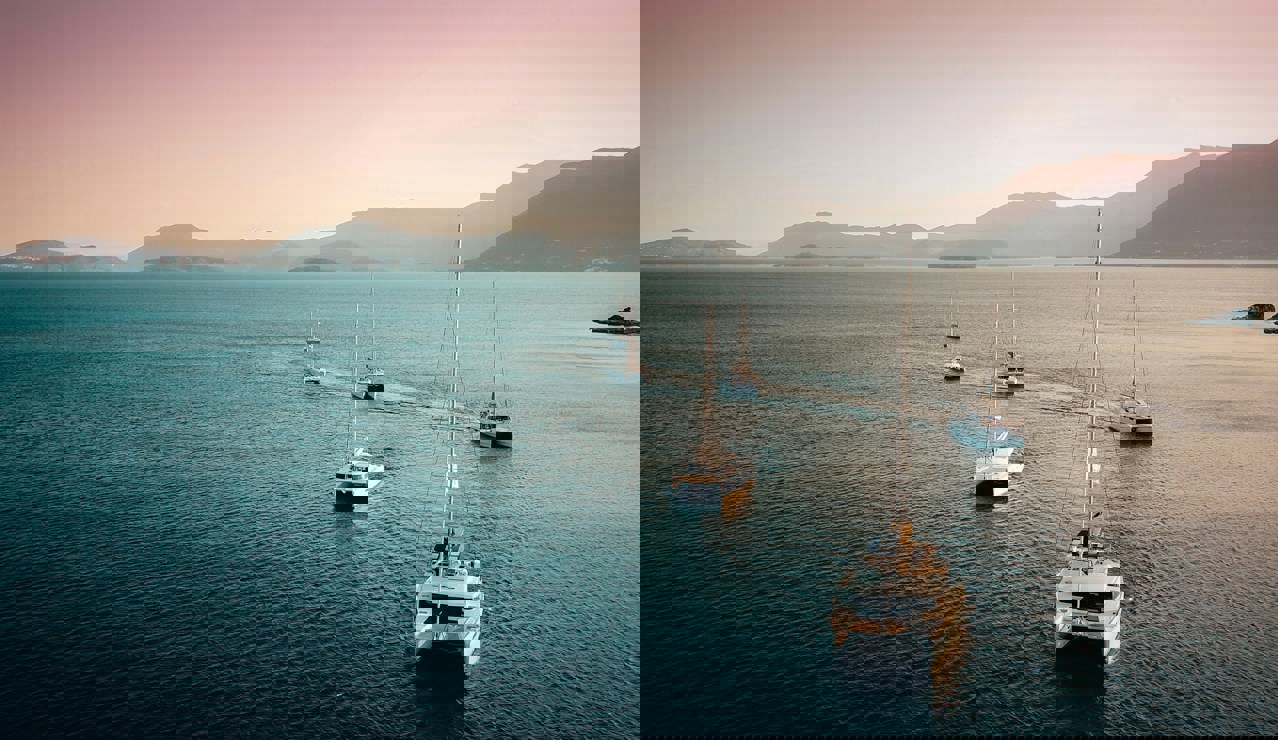 Several sailboats and catamarans sailing in formation across calm blue water at sunset, with mountains and islands in the distance under a pink and golden sky.