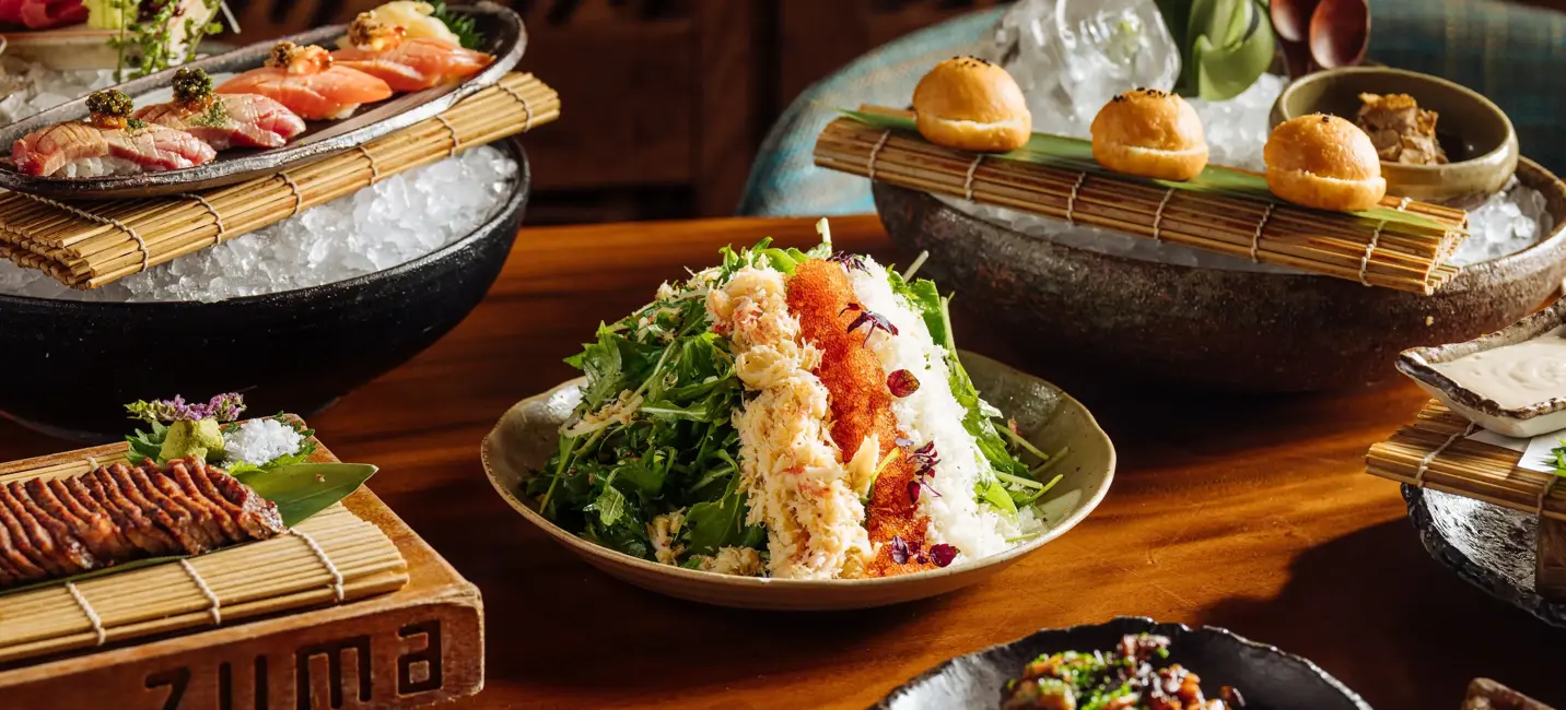 Assorted Japanese dishes including sushi, salad, and appetizers beautifully presented on a wooden table at Zuma restaurant.
