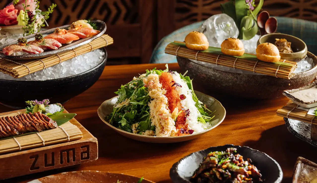 Assorted Japanese dishes including sushi, salad, and appetizers beautifully presented on a wooden table at Zuma restaurant.