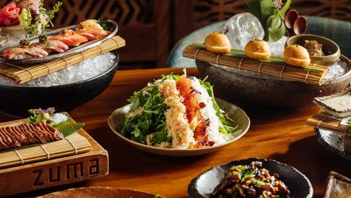 Assorted Japanese dishes including sushi, salad, and appetizers beautifully presented on a wooden table at Zuma restaurant.