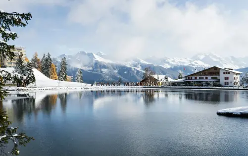 Scenic winter view of Crans-Montana with snowy mountains, lake reflection, and alpine hotels.