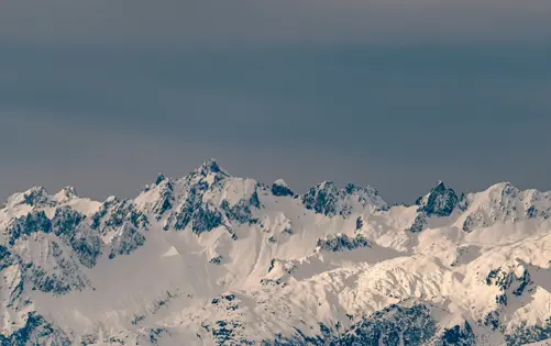 Panoramic view of snow-covered mountain peaks under a moody gray sky.