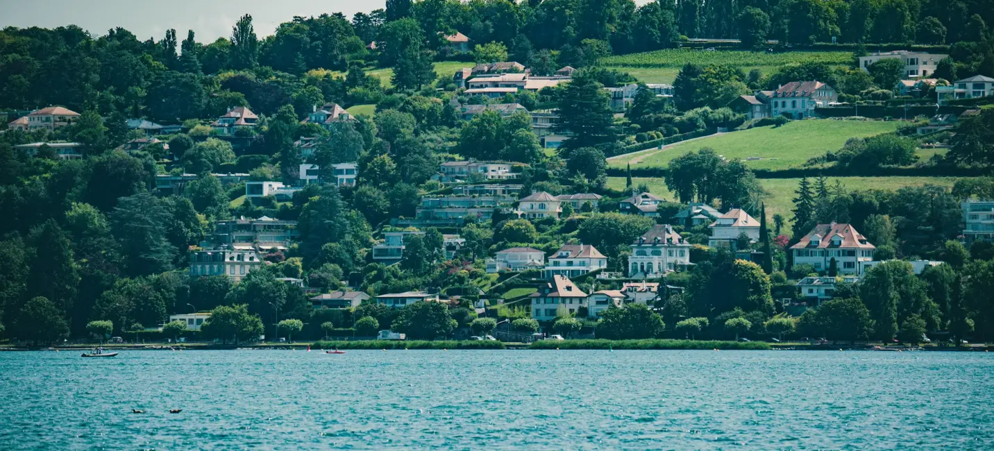 فيلات أنيقة على سفح التل تطل على بحيرة زرقاء هادئة، تحيط بها خضرة وارفة تحت سماء صيفية ناعمة.