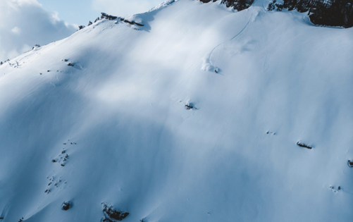 Snow-covered mountain peak with steep slopes and rocky cliffs under a blue sky.