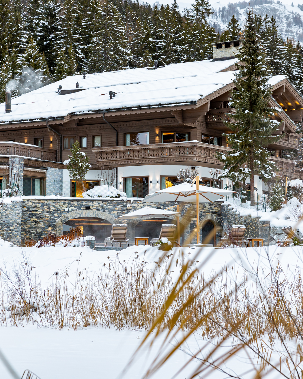 Luxury wooden chalet surrounded by snow-covered trees in a winter mountain landscape.
