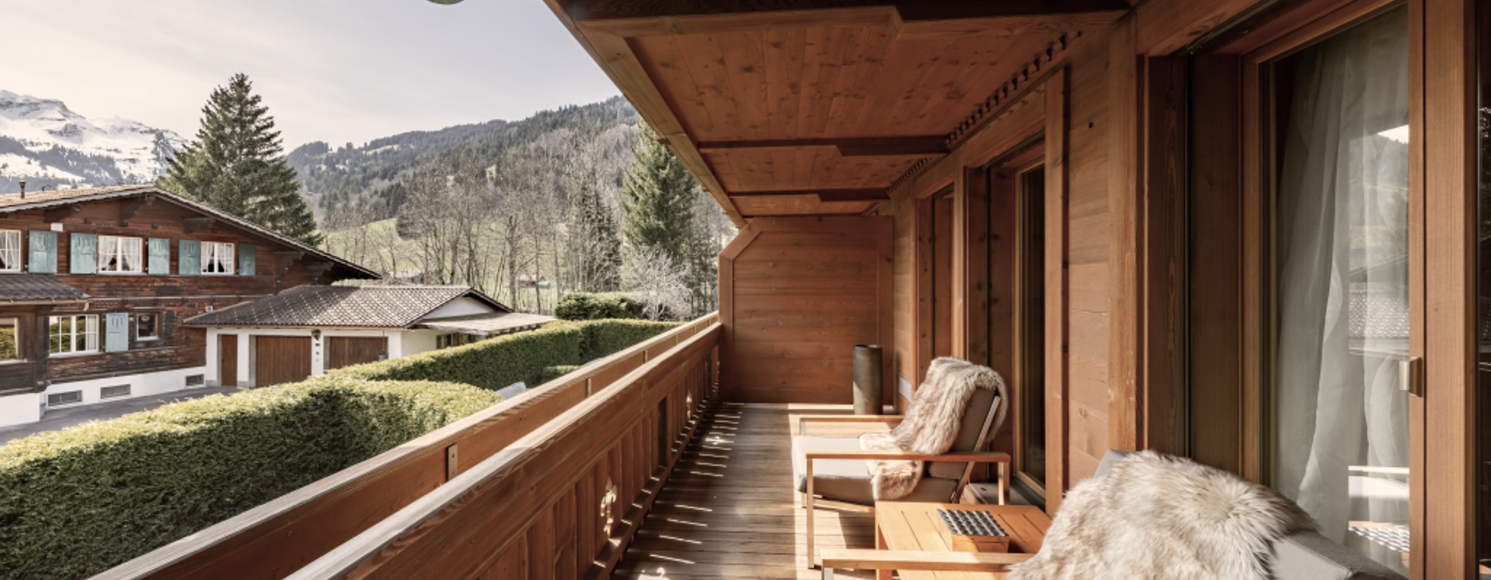 Wooden balcony with cozy fur-covered chairs overlooking alpine chalets and snow-capped mountains at Ultima Gstaad.