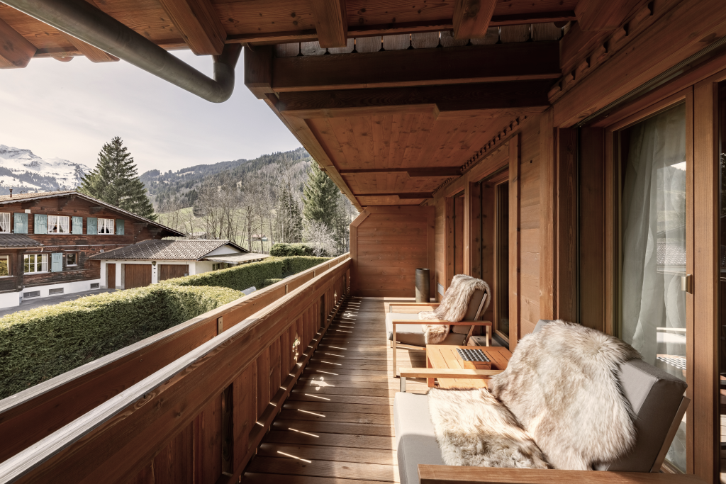 Wooden balcony with cozy fur-covered chairs overlooking alpine chalets and snow-capped mountains at Ultima Gstaad.