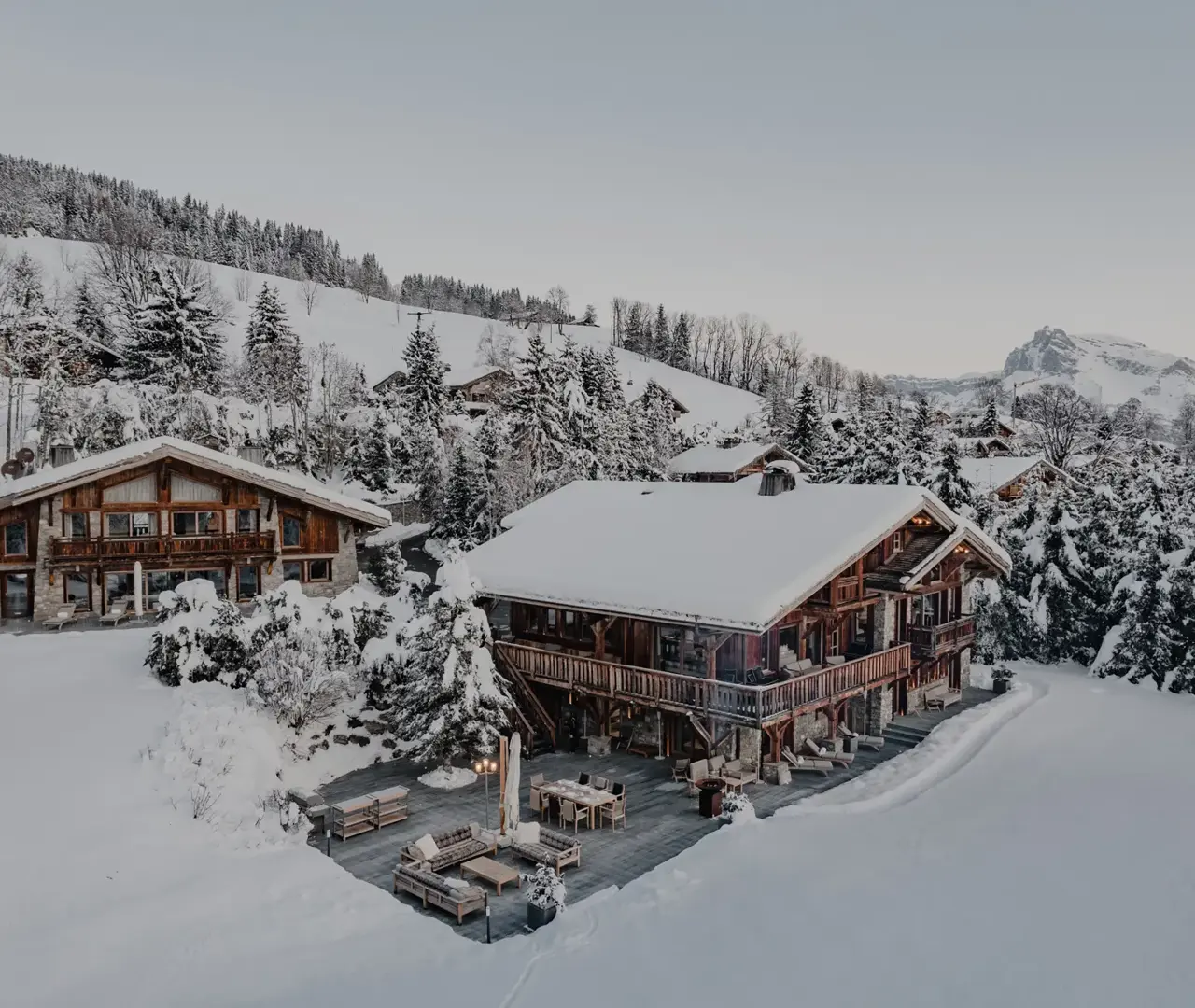 Luxury alpine chalet surrounded by snow-covered trees and mountain views at dusk.