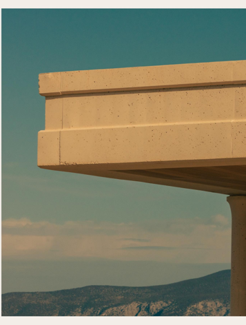 Modern architectural structure with concrete overhang against a clear sky and mountain backdrop.