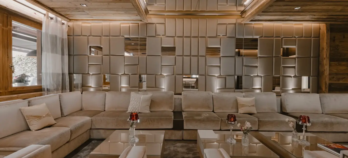 صالة فاخرة تحتوي على أرائك بيج ناعمة وجدران مزخرفة بتصميم هندسي عاكس ولمسات خشبية دافئة، مما يضفي أجواءً أنيقة ومريحة.