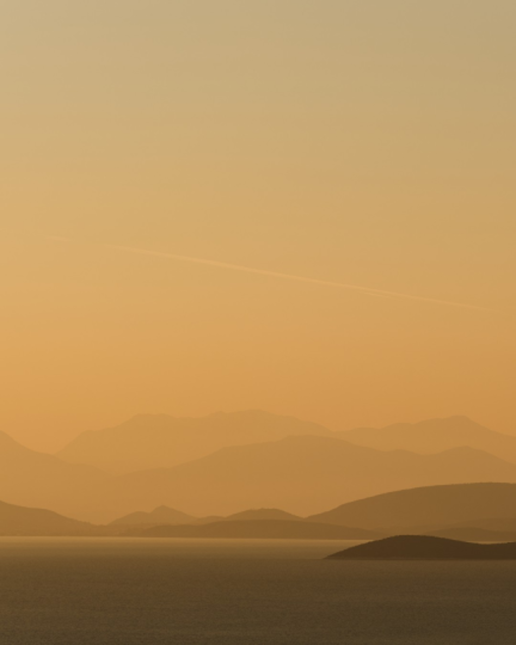 Serene coastal landscape with layered mountain silhouettes at sunset over calm sea.