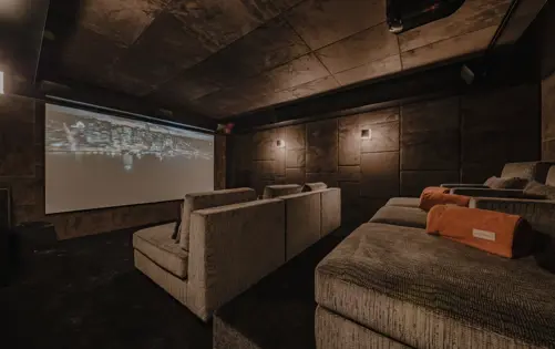Salle de cinéma privée dans un chalet alpin de luxe, avec sièges confortables sur plusieurs niveaux, éclairage d’ambiance chaleureux et grand écran de projection pour une expérience cinéma exclusive en montagne.
