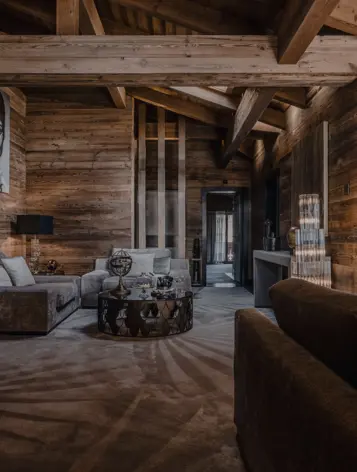 A luxurious chalet-style lounge with wooden walls and exposed beams, featuring plush velvet sofas, a sculptural coffee table, and warm ambient lighting that enhances the natural textures.