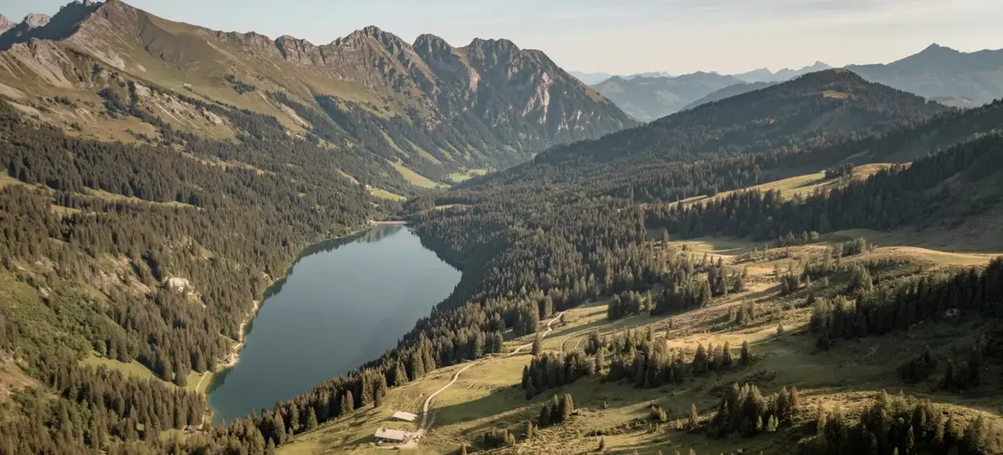 Breathtaking alpine landscape with a serene lake surrounded by pine forests and rugged mountain peaks under a soft blue sky.