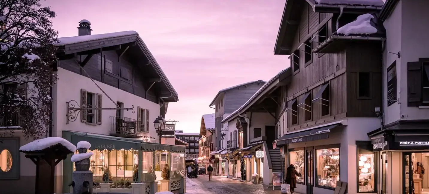 A serene alpine village street glows under a soft pink twilight, its snow-dusted rooftops and warmly lit boutiques inviting quiet evening strolls.