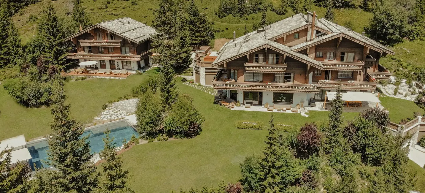 A luxury alpine chalet with expansive terraces, manicured gardens, and a private pool surrounded by pine trees.